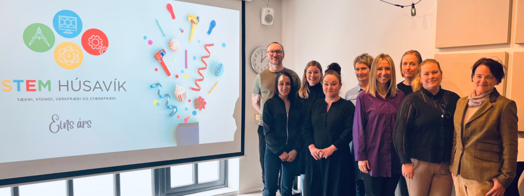 A projected presentation shows the STEM Húsavík logo with colorful STEM icons and celebratory graphics, with team members lined up next to it.